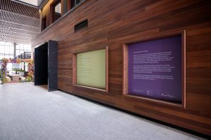 Two large vinyl installations hang against a wood-paneled wall. The installation on the left is a poem, and the installation on the right displays information about the project.