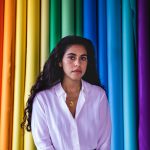 A woman, journalist and artist Mona Chalabi, poses in front of a colorful rainbow background
