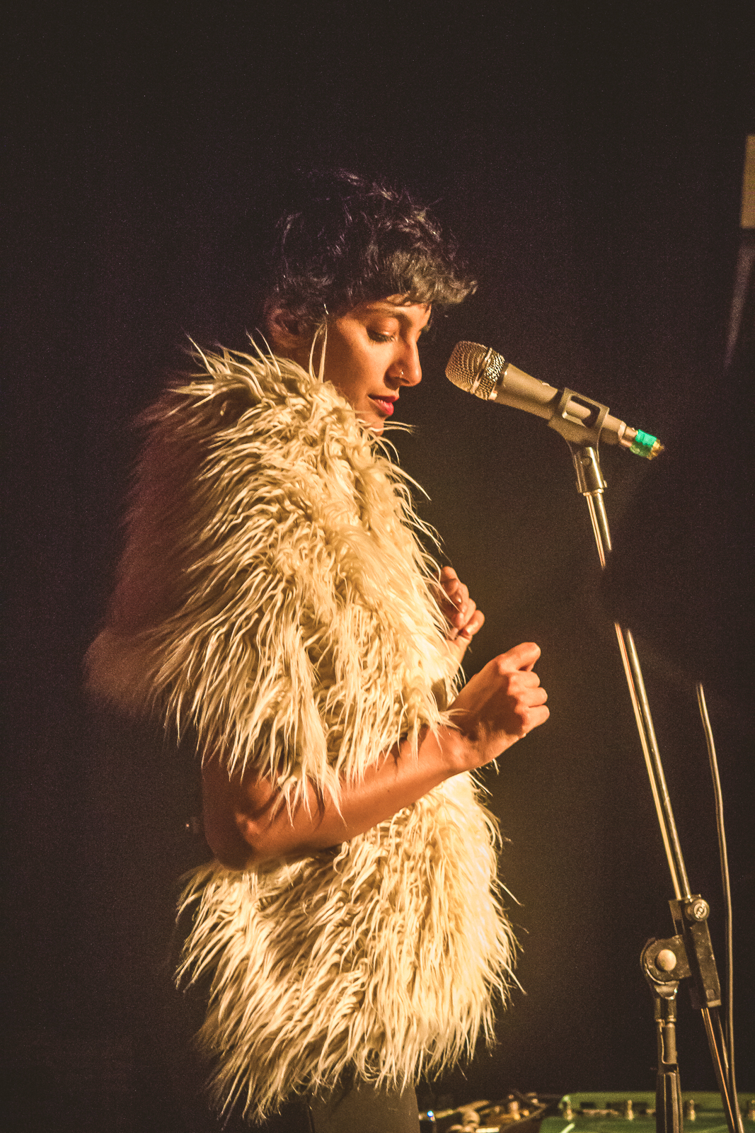 This picture shows Samita Sinha standing in front of a microphone. Samita is wearing a big furry white short sleeved jacket.