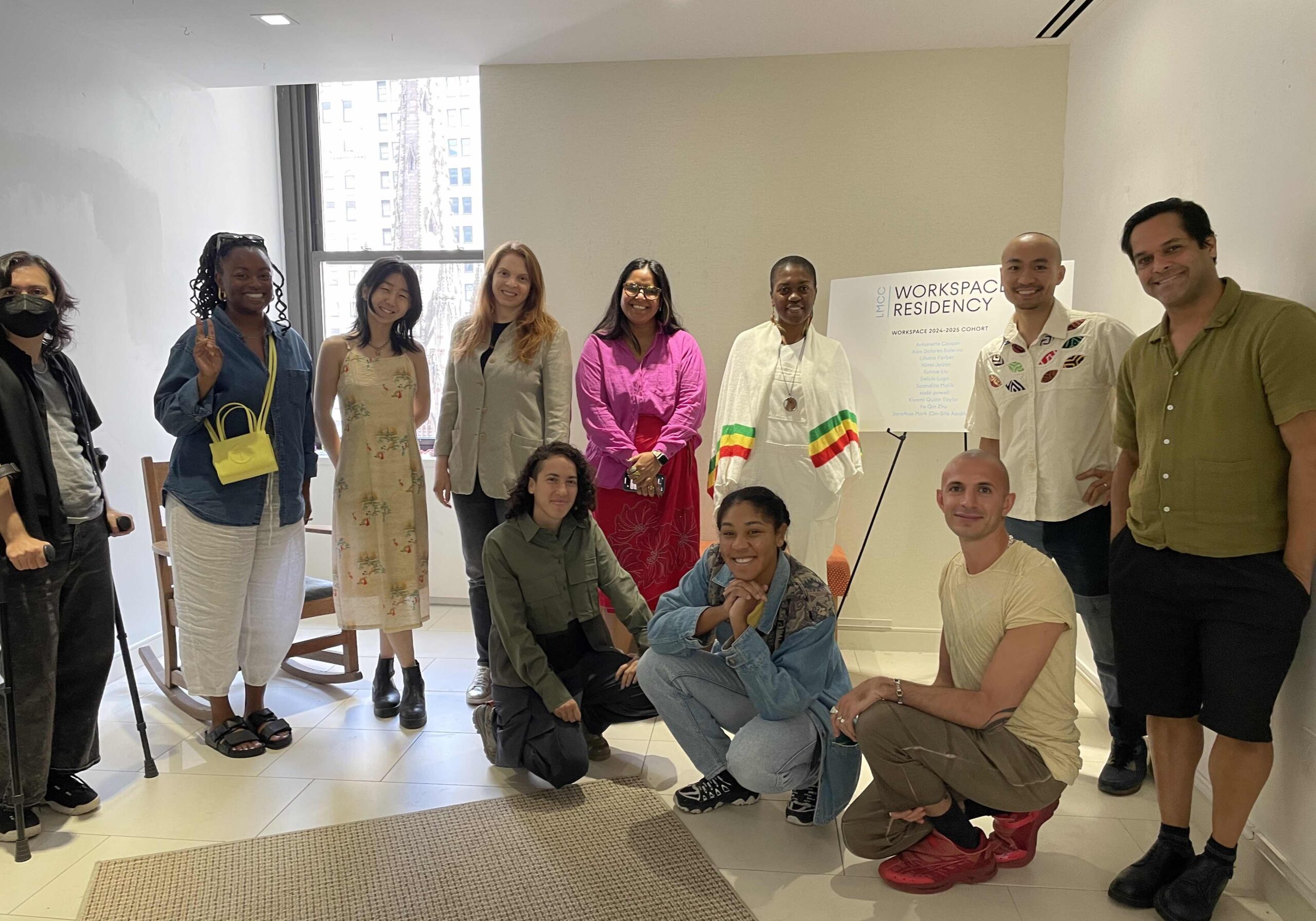 A group of 11 artists of various genders and racial identities with colorful clothing smiling and posing for a picture in an indoor space. Three individual are sitting in the foreground: SaraNoa Mark, Kiyomi Quinn Taylor and Nima Jeizan (from left to right), and eight individuals are standing behind in a semi circle: Alex Dolores Salerno, sadé powell, Sunnie Liu, Liliana Farber, Spandita Malik, Antoinette Cooper, Ye Qin Zhu, and Delvin Lugo (from left to right).